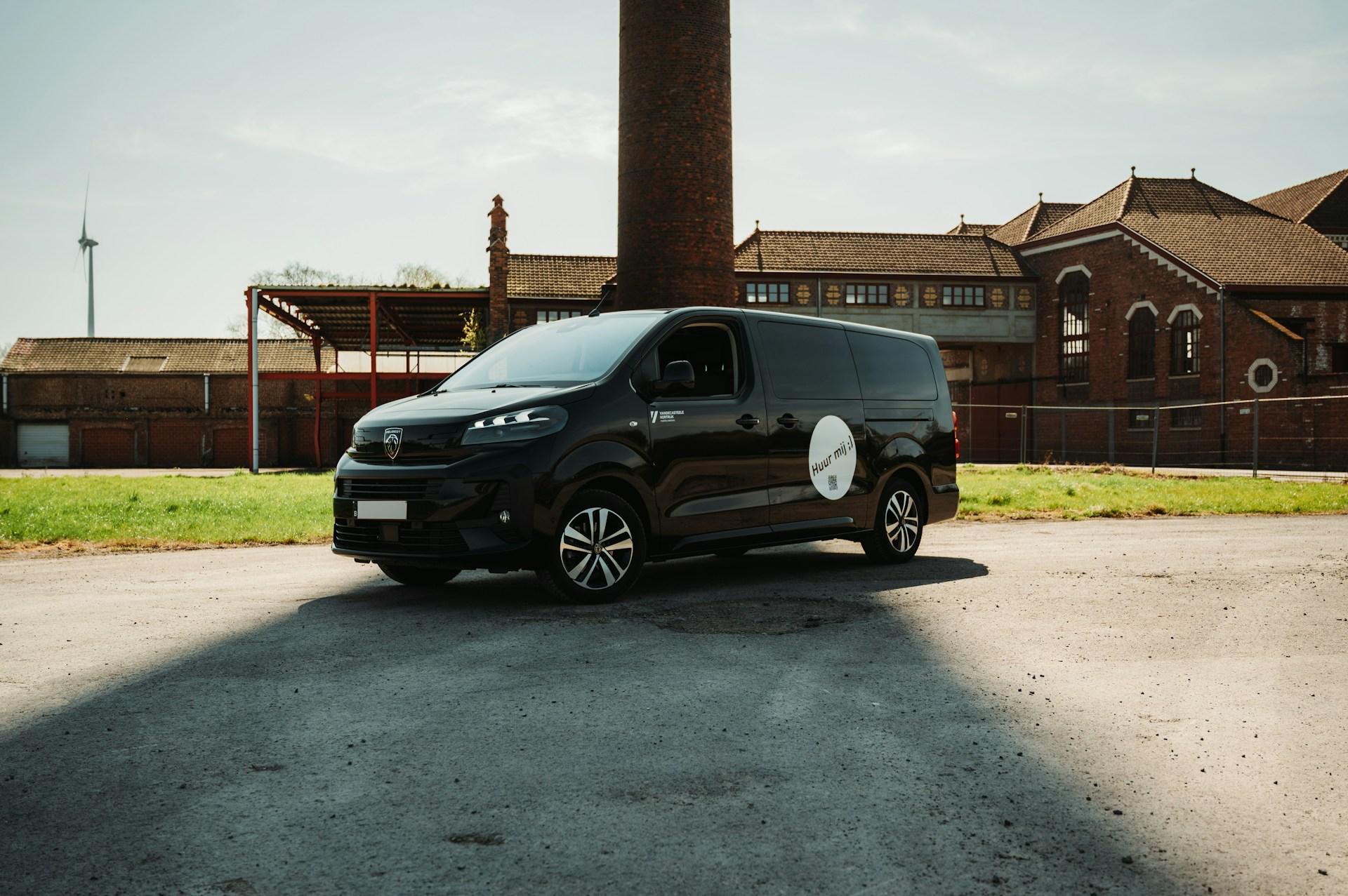 Black 12-seat van parked in front of an industrial building