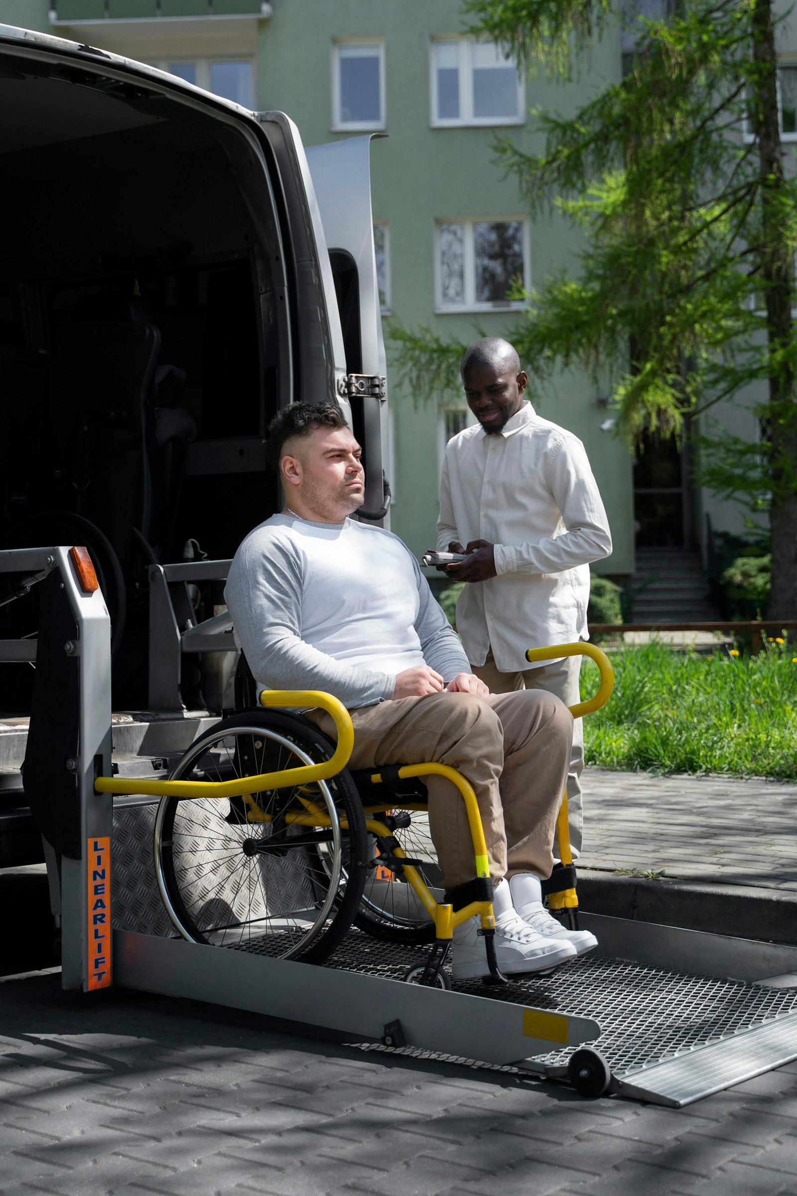 Passenger in a wheelchair boarding an accessible van via ramp, assisted by a support worker