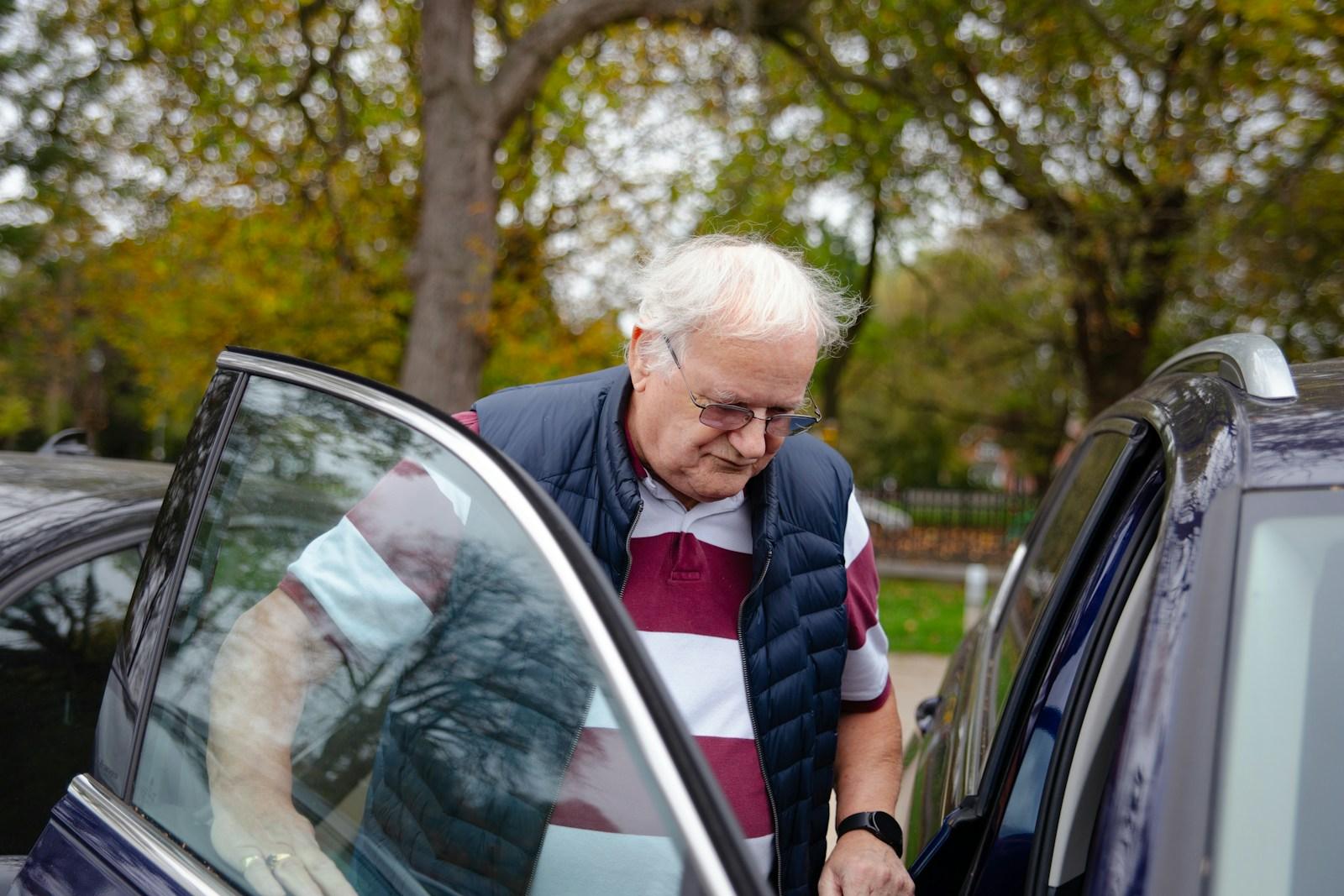 Older passenger being helped into the back of a sedan on a tree-lined Sydney street